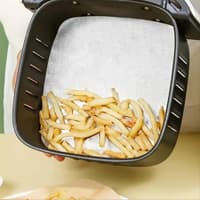 Еър фрайър кошница, постлана с подложка и порция пържени картофи върху нея

